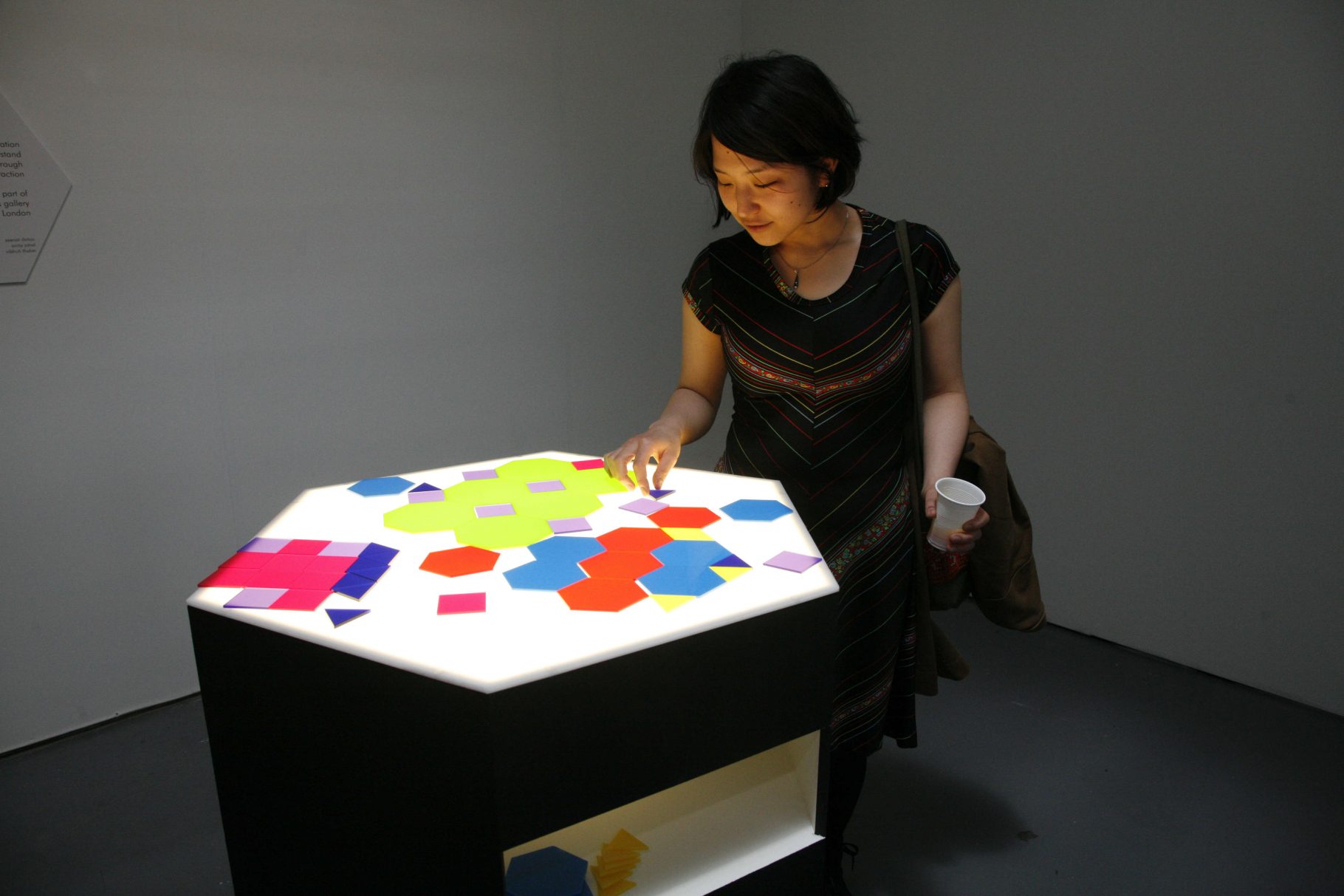 A woman arranges coloured hexagons on an illuminated plinth