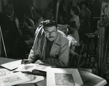 Photograph showing a student, identified as Douglas Sutton, sketching from books and prints, with men and women students working at easels behind him. Some of the students' work can be seen.